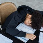 tired black man lying on opened book and homework papers